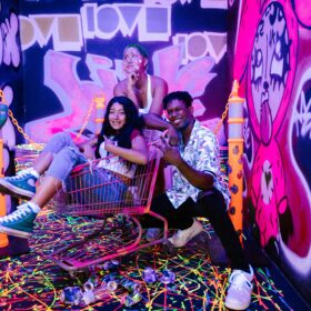 Grupo de jóvenes con maquillaje artístico y actitud creativa en un espacio urbano con grafiti, luces neón y arte callejero